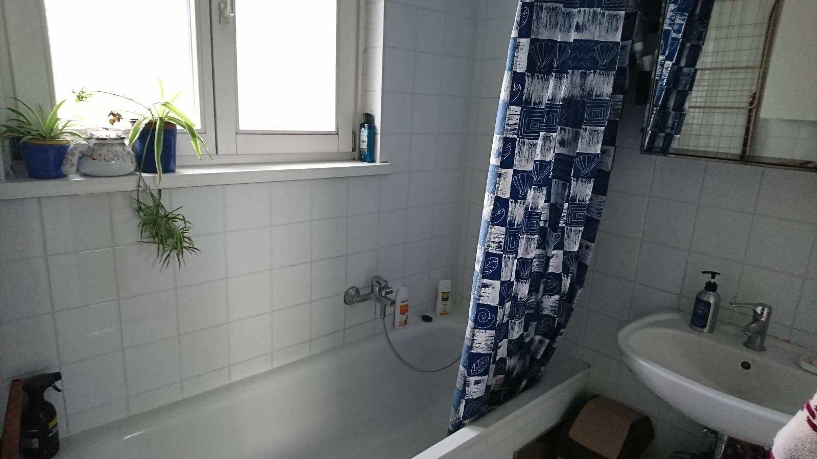 Badezimmer mit Badewanne, Waschbecken, Spiegel und einem Fenster, das für natürliche Belüftung sorgt.