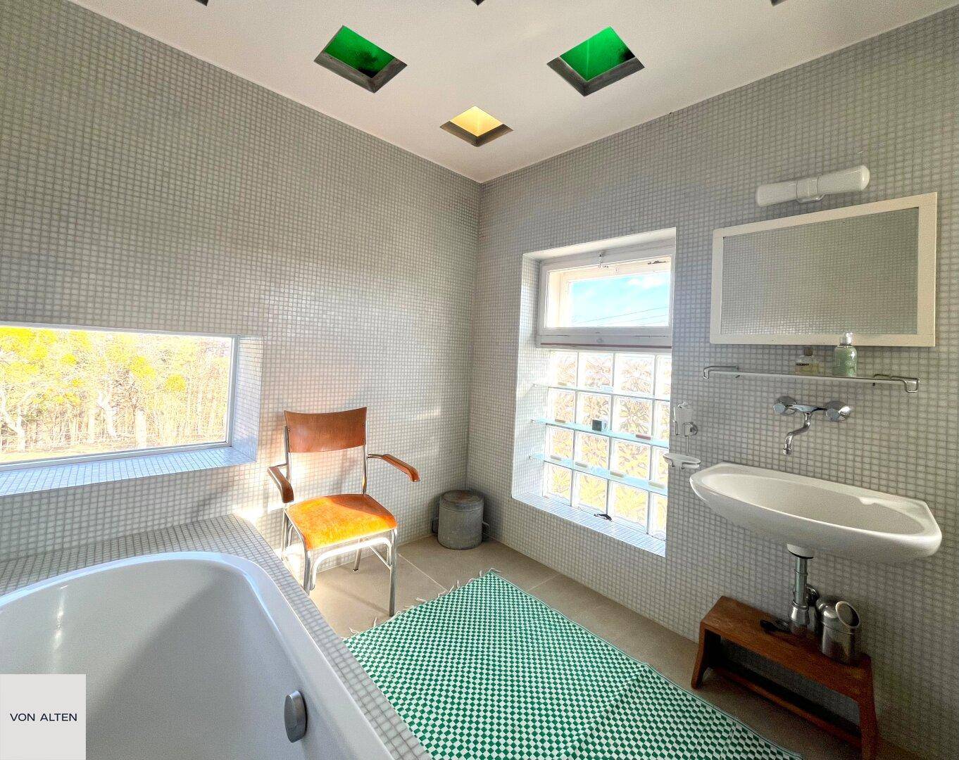Helles Badezimmer mit Badewanne, Mosaikfliesen und zwei Fenstern für viel Tageslicht.