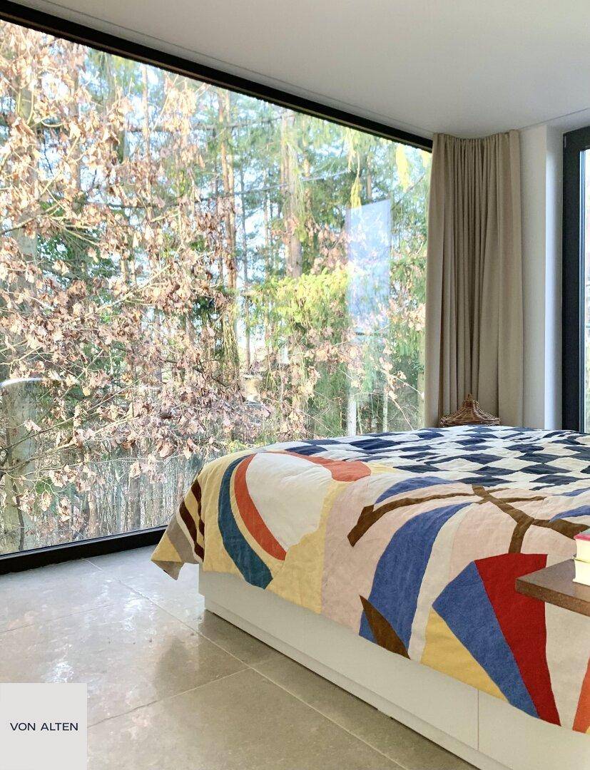 Schlafzimmer mit großem Fenster, das einen direkten Blick auf die umliegenden Bäume bietet.
