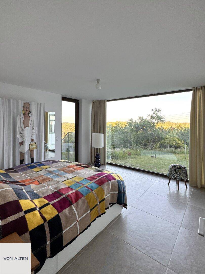 Helles Schlafzimmer mit großem Bett, farbenfroher Decke und weitem Blick in die Natur.