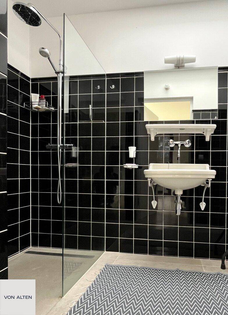 Modernes Badezimmer mit schwarzen Fliesen, Duschkabine und weißem Waschbecken.
