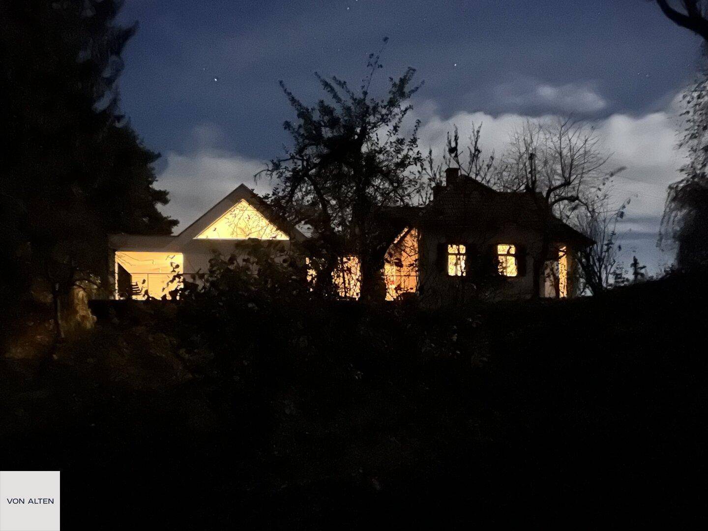 Hausansicht bei Nacht mit beleuchteten Fenstern und dunklem Himmel.