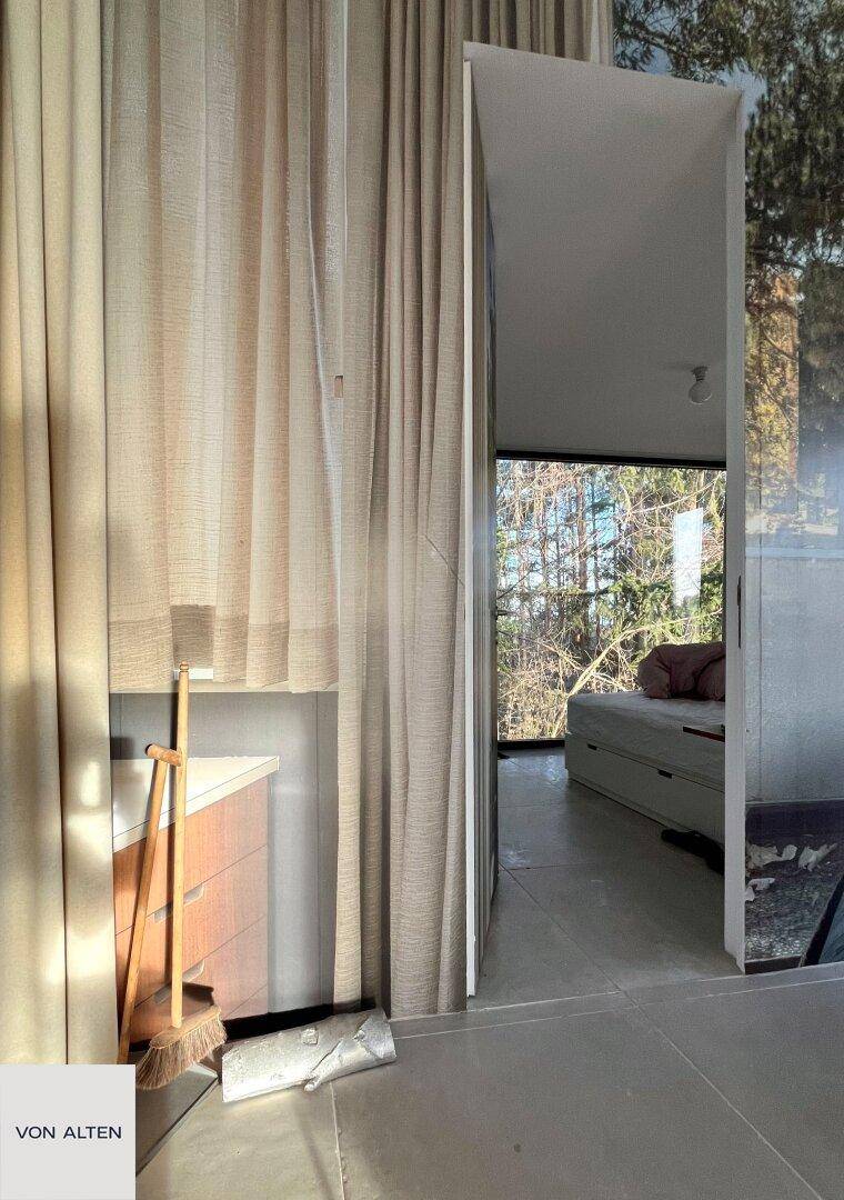 Schlafzimmer mit bodentiefen Fenstern und Vorhängen, die viel Tageslicht hereinlassen.