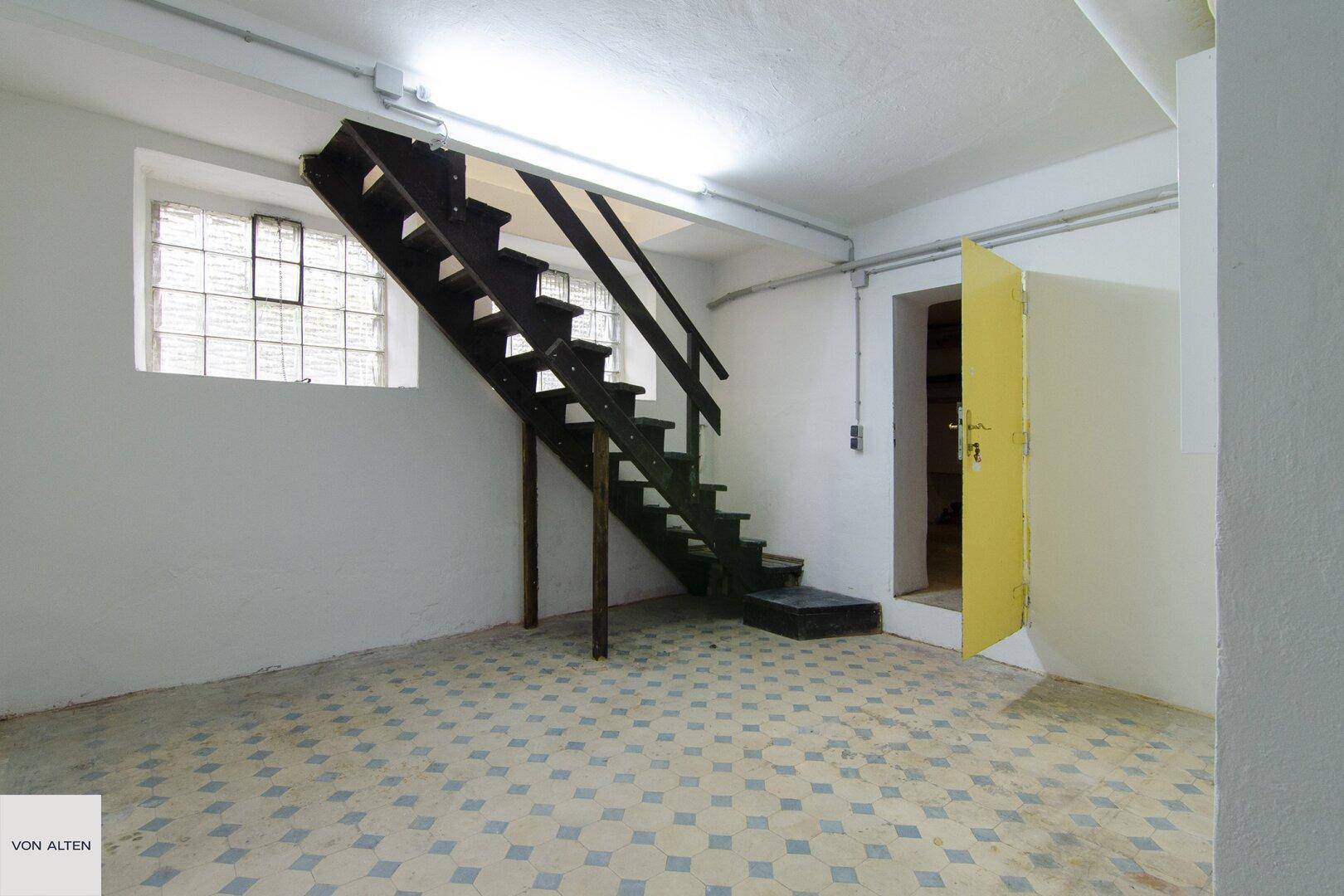 Kellerraum mit gemustertem Fliesenboden und Zugang über eine Holztreppe, ideal als Stauraum.