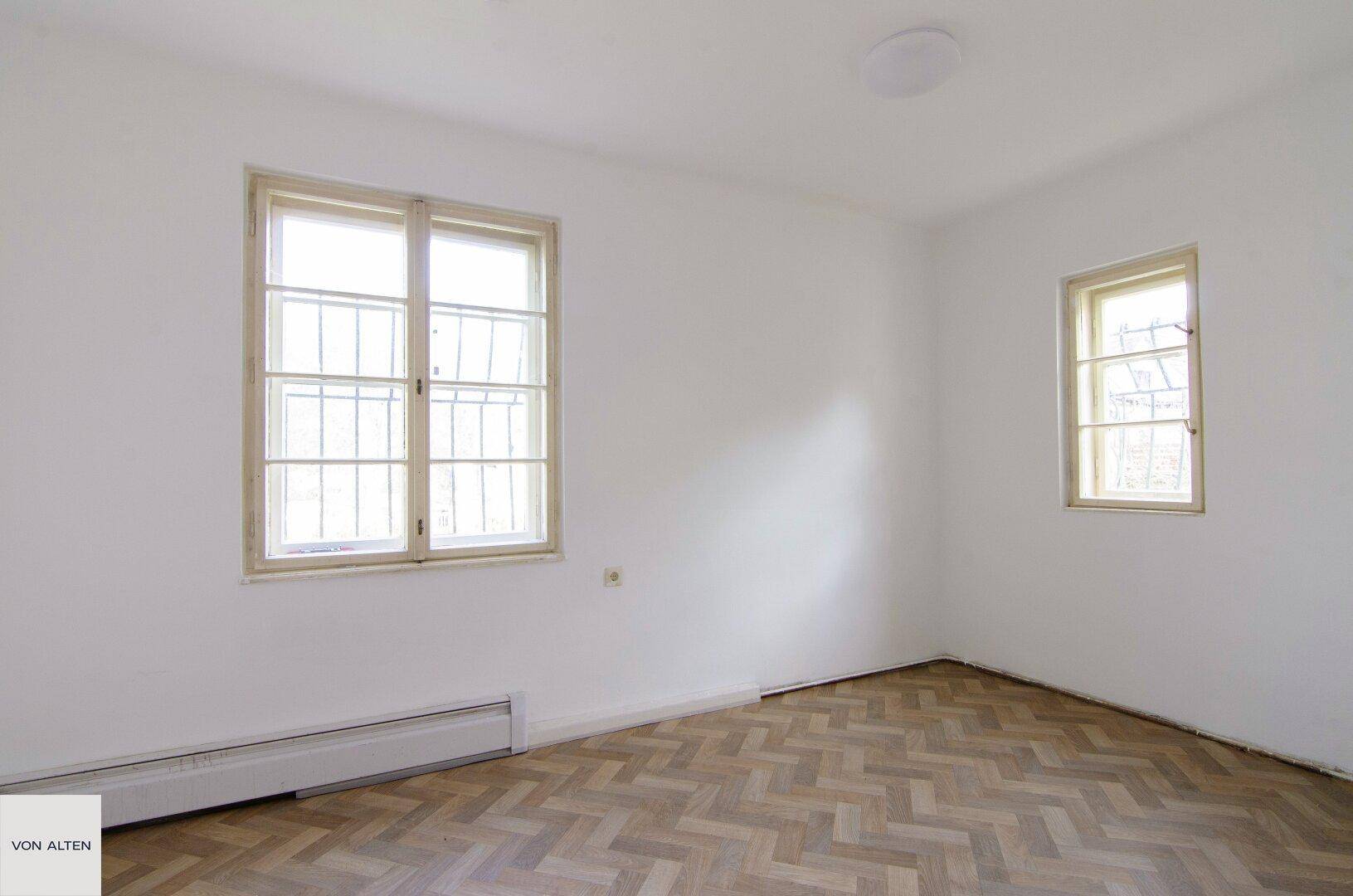 Helles Schlafzimmer mit klassischem Fischgrätparkett und großen Fenstern.