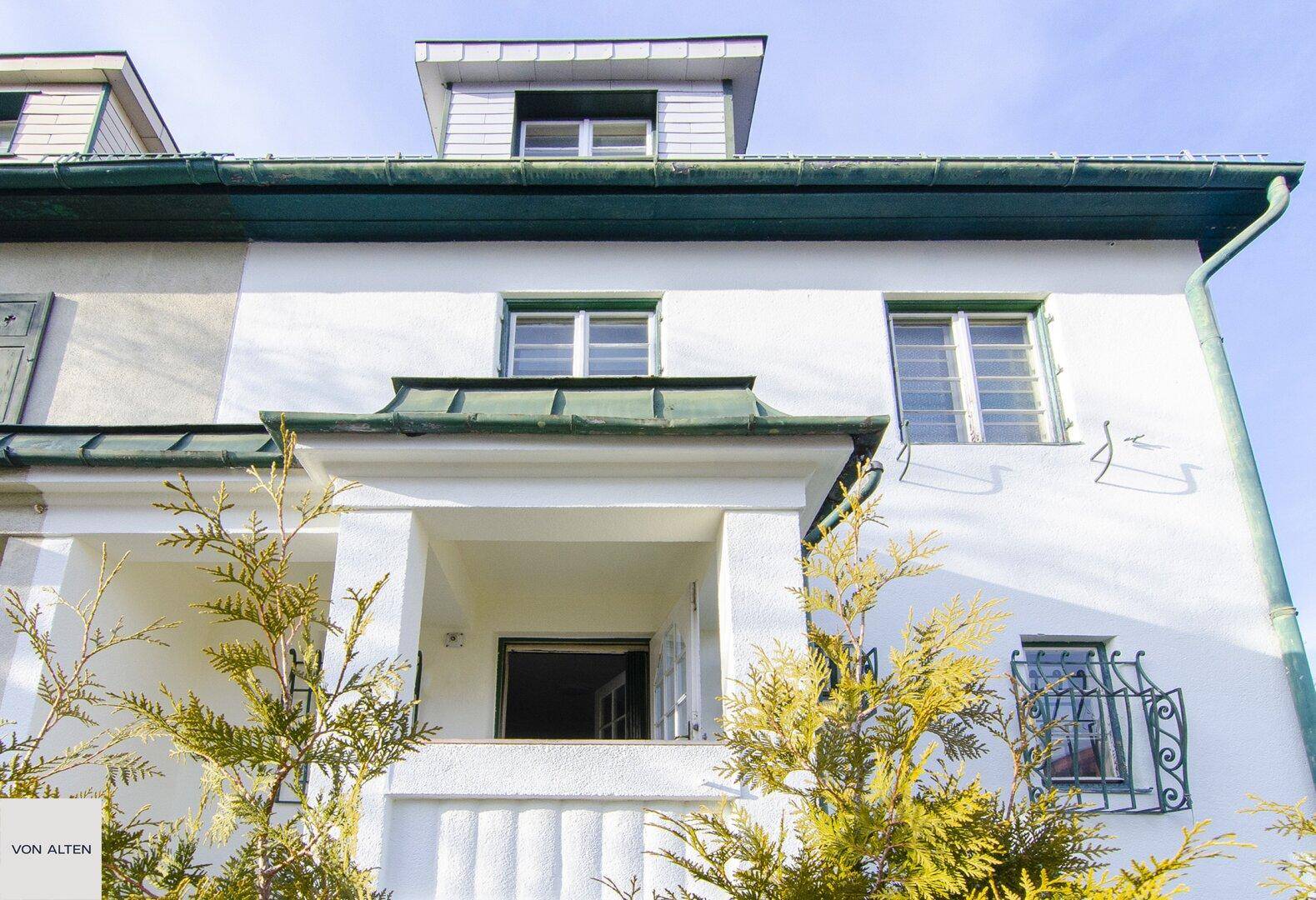 Detailansicht der Fassade mit überdachtem Eingangsbereich und dekorativen Fenstergittern.