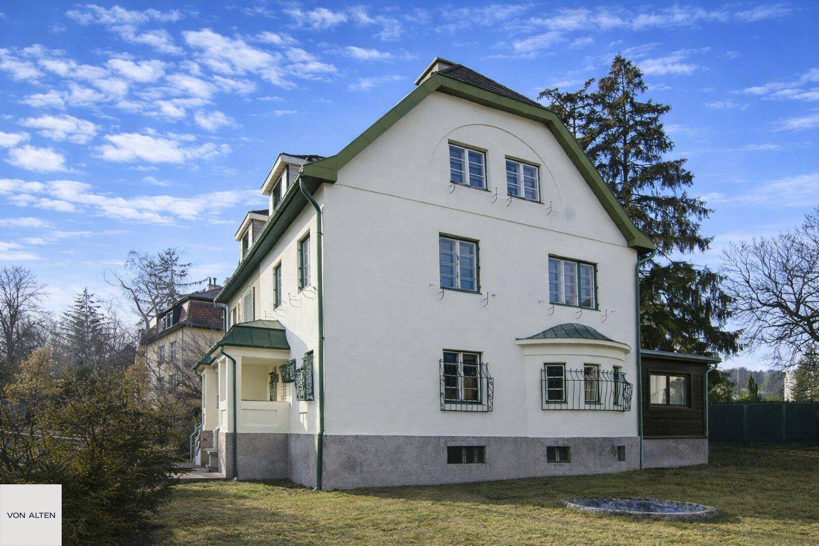 Seitenansicht des Hauses mit weißer Fassade, grünen Akzenten und weitläufigem Rasenbereich.