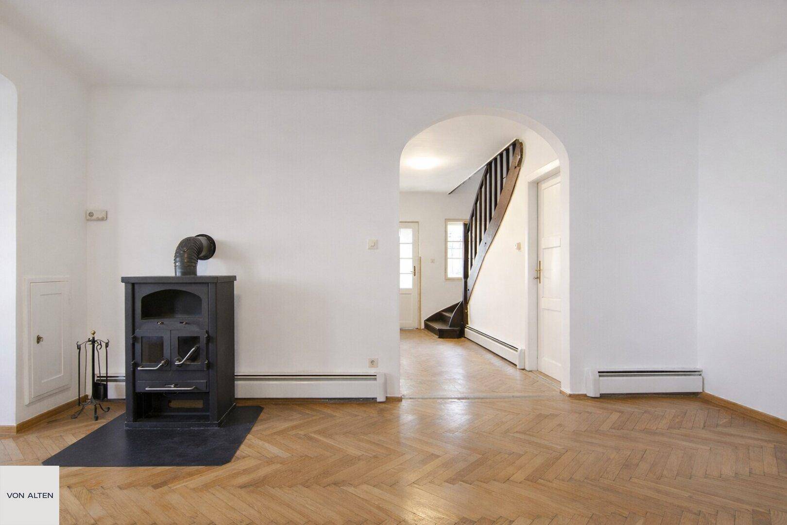 Geräumiges Wohnzimmer mit Holzofen und offenem Durchgang zum Treppenhaus.
