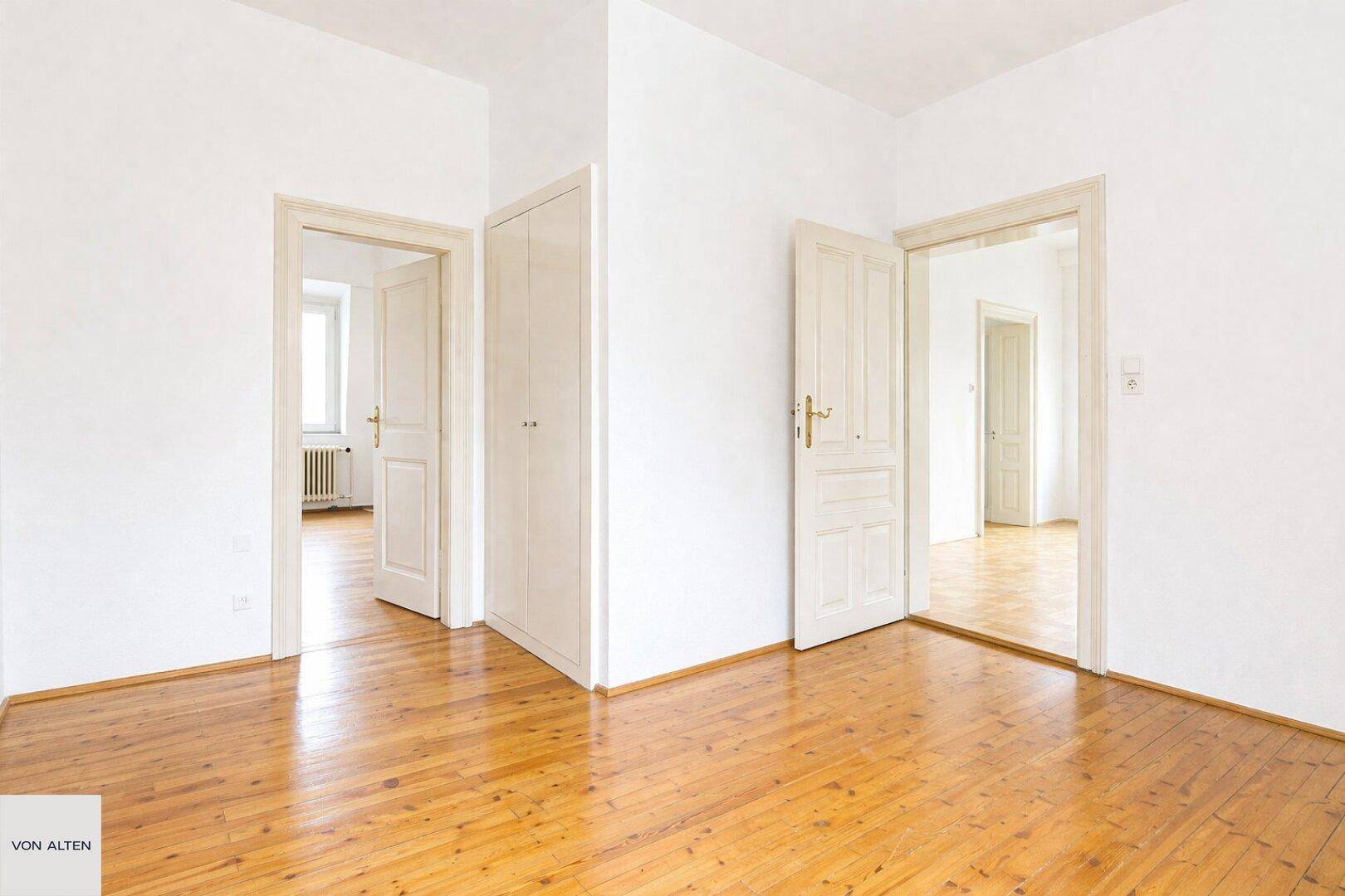 Innenraum mit Holzboden und mehreren Türen, der verschiedene Räume miteinander verbindet.