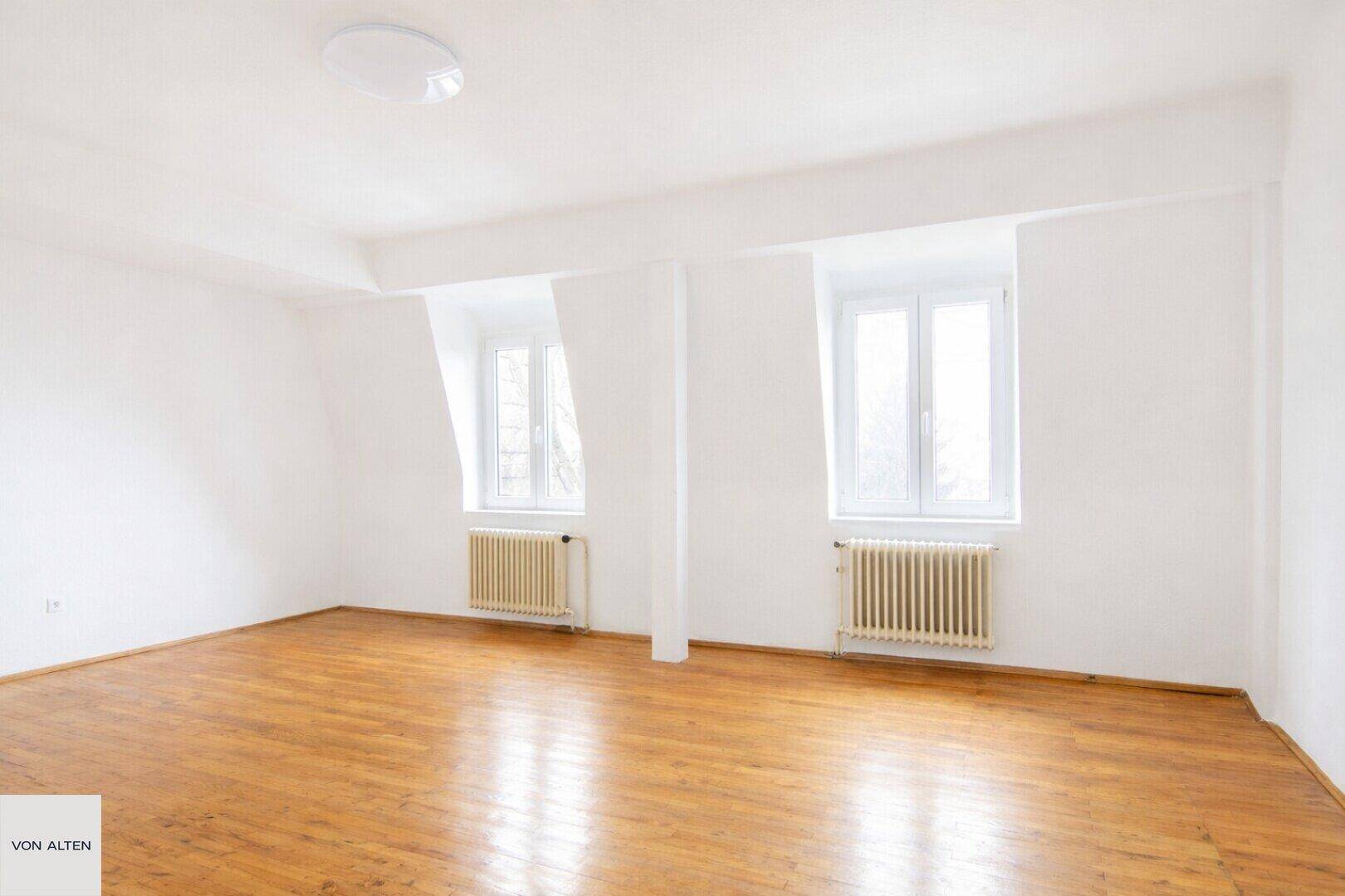 Geräumiges Zimmer mit Holzboden und zwei Fenstern, ideal als Schlaf- oder Arbeitszimmer im Dachgeschoss.