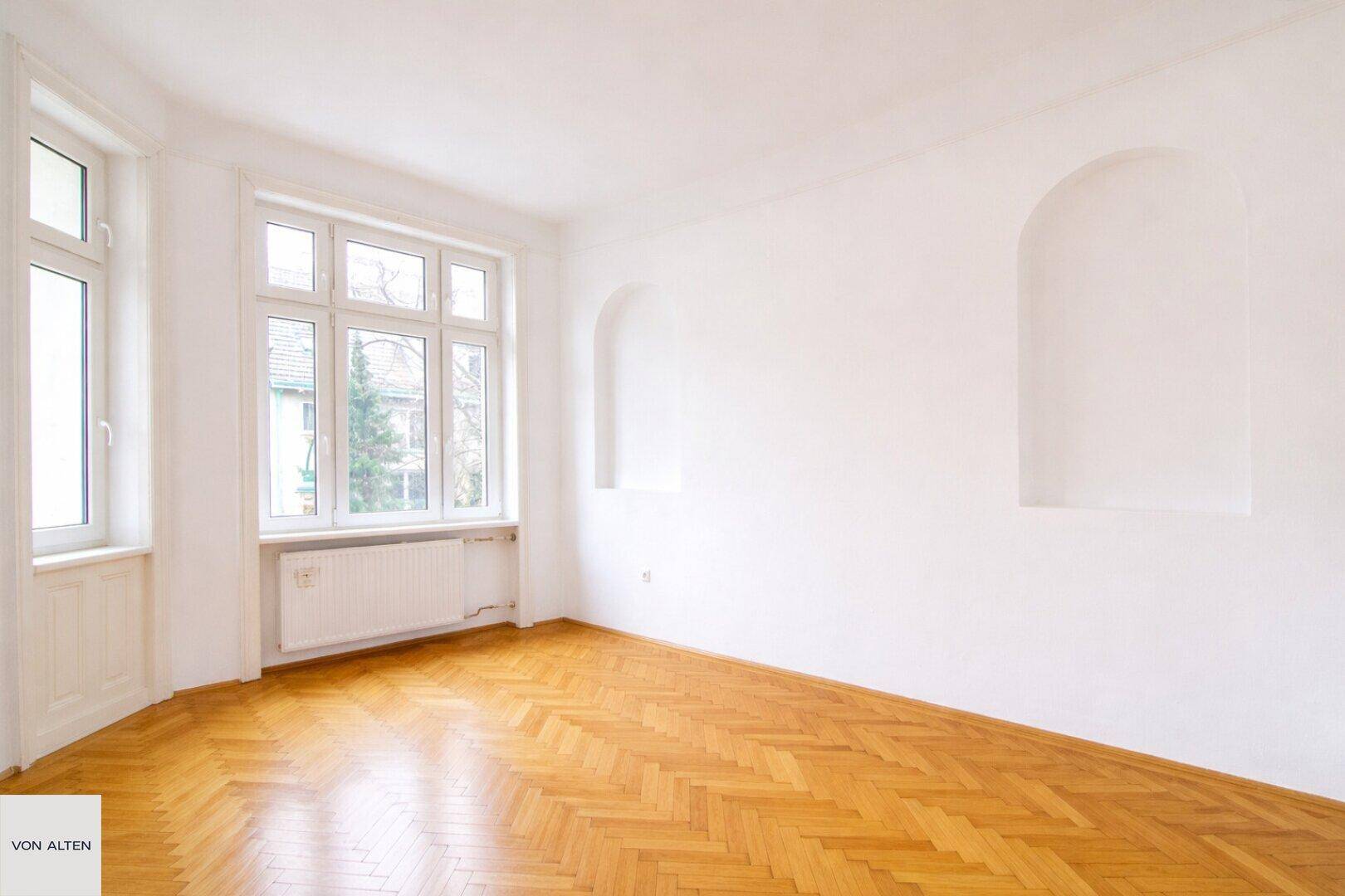 Geräumiges Zimmer mit Holzboden, großen Fenstern und dekorativen Wandnischen, bietet viel Licht.