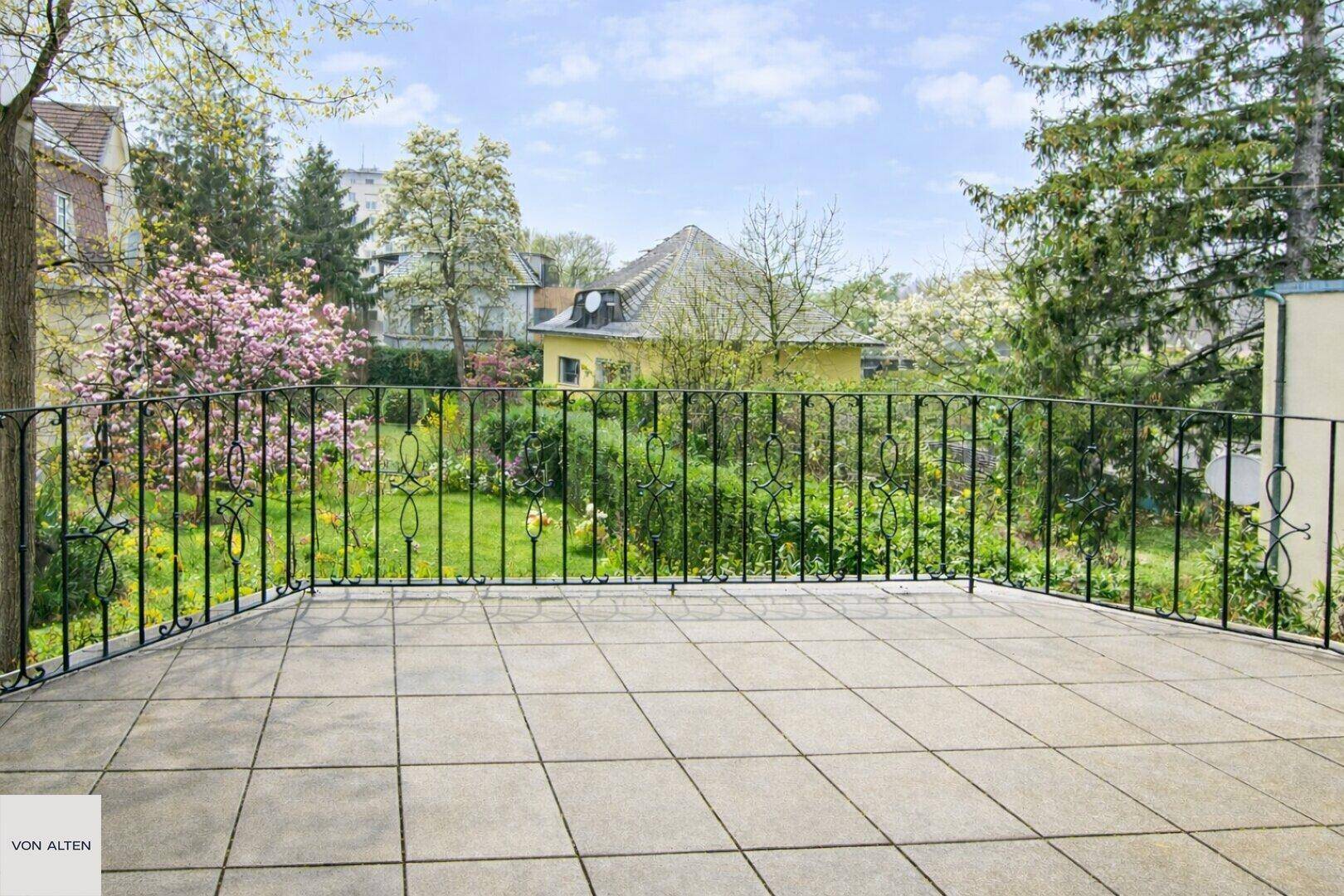 Großer Balkon mit Fliesenboden und schmiedeeisernem Geländer, mit Blick auf den grünen Garten.