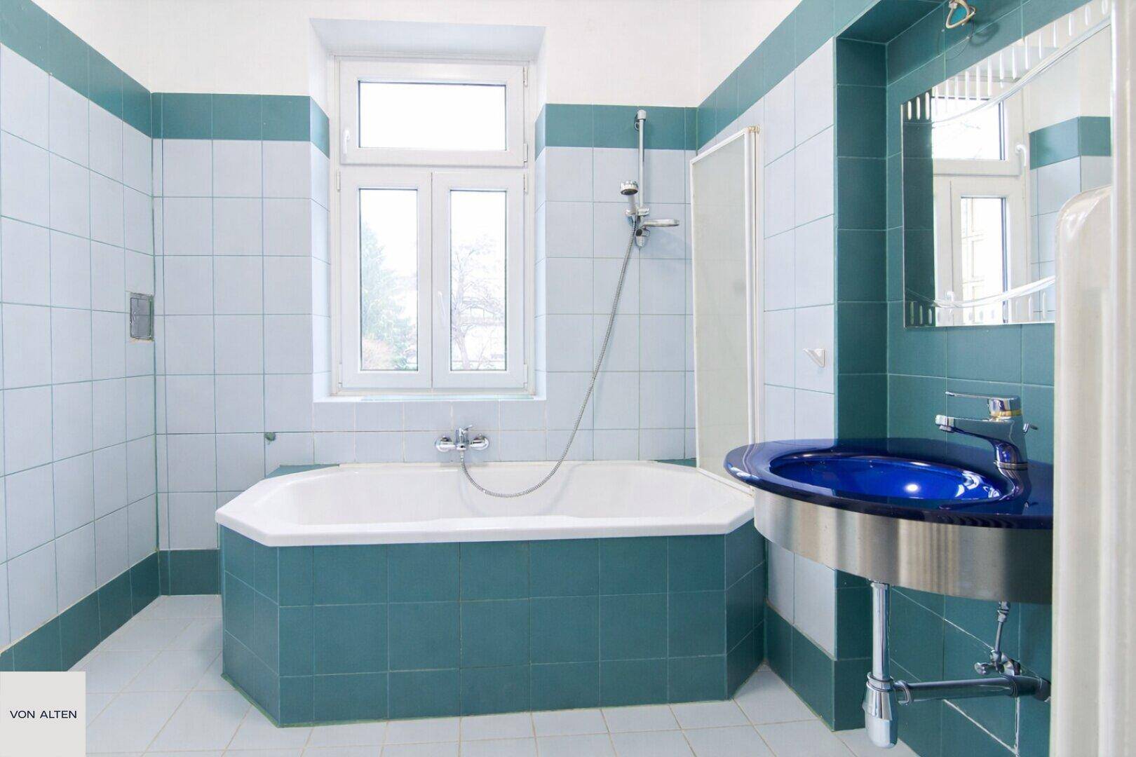 Badezimmer mit blauen und weißen Fliesen, Badewanne und Fenster, im Stil der 80er Jahre.