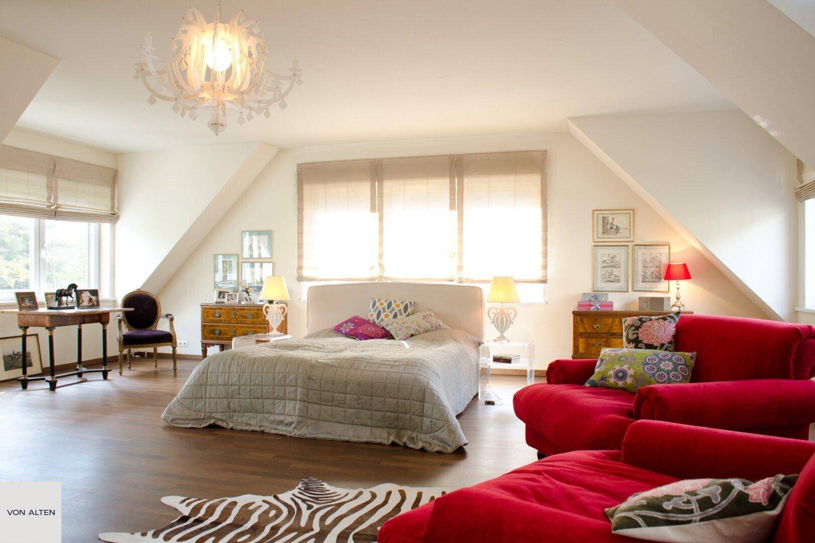Geräumiges Schlafzimmer im Dachgeschoss mit rotem Sofa, Doppelbett und Holzboden.