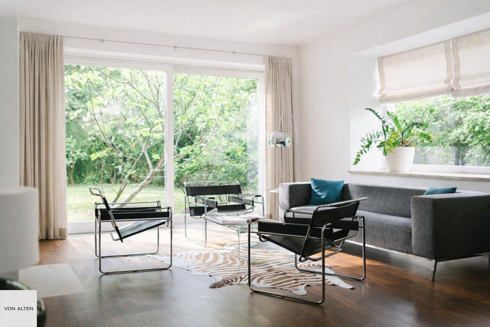 Helles Wohnzimmer mit großen Fenstern, Holzboden und modernem Mobiliar.