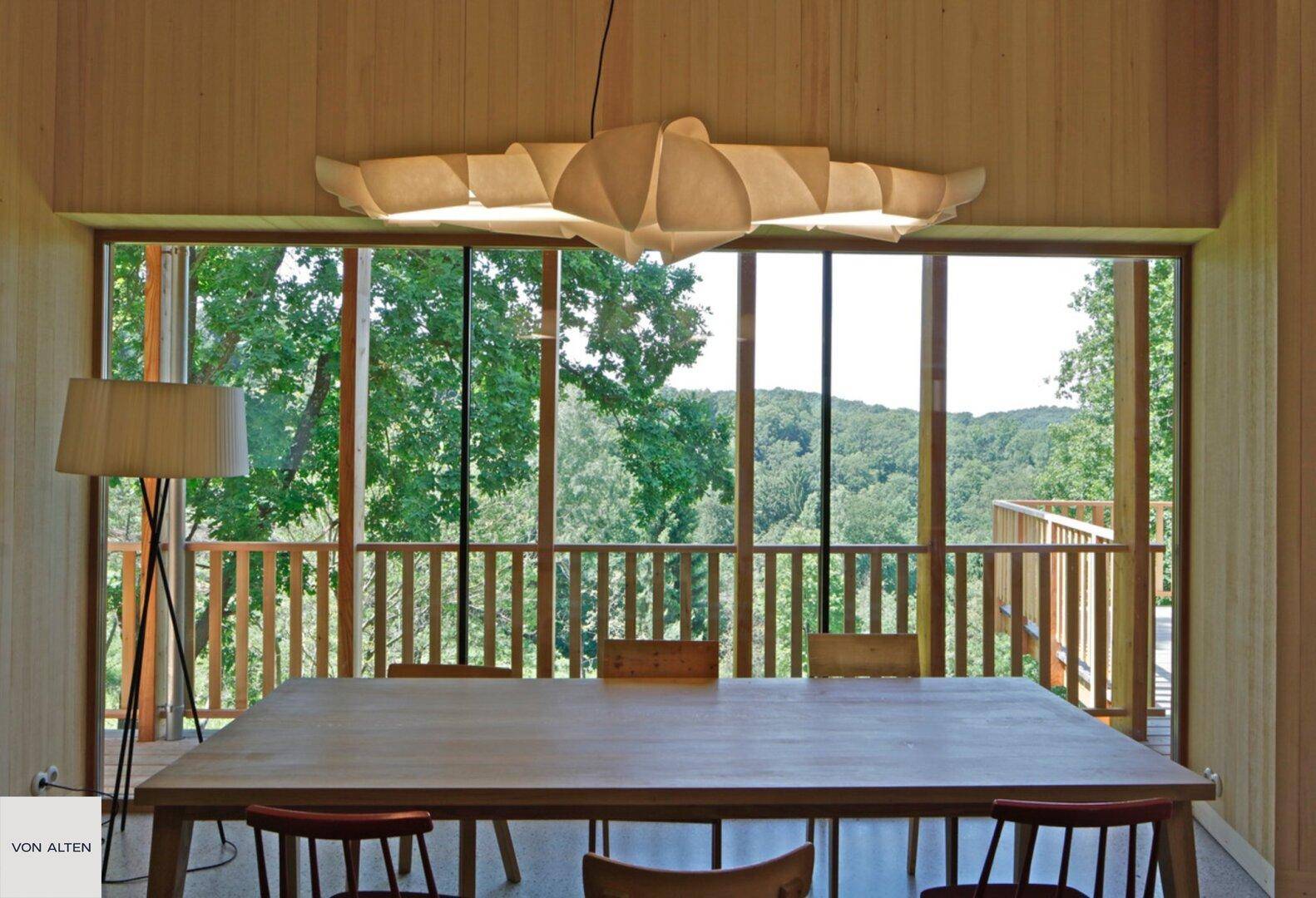 Heller Essbereich mit Holztisch und Stühlen, großen Fenstern und weitem Waldblick.