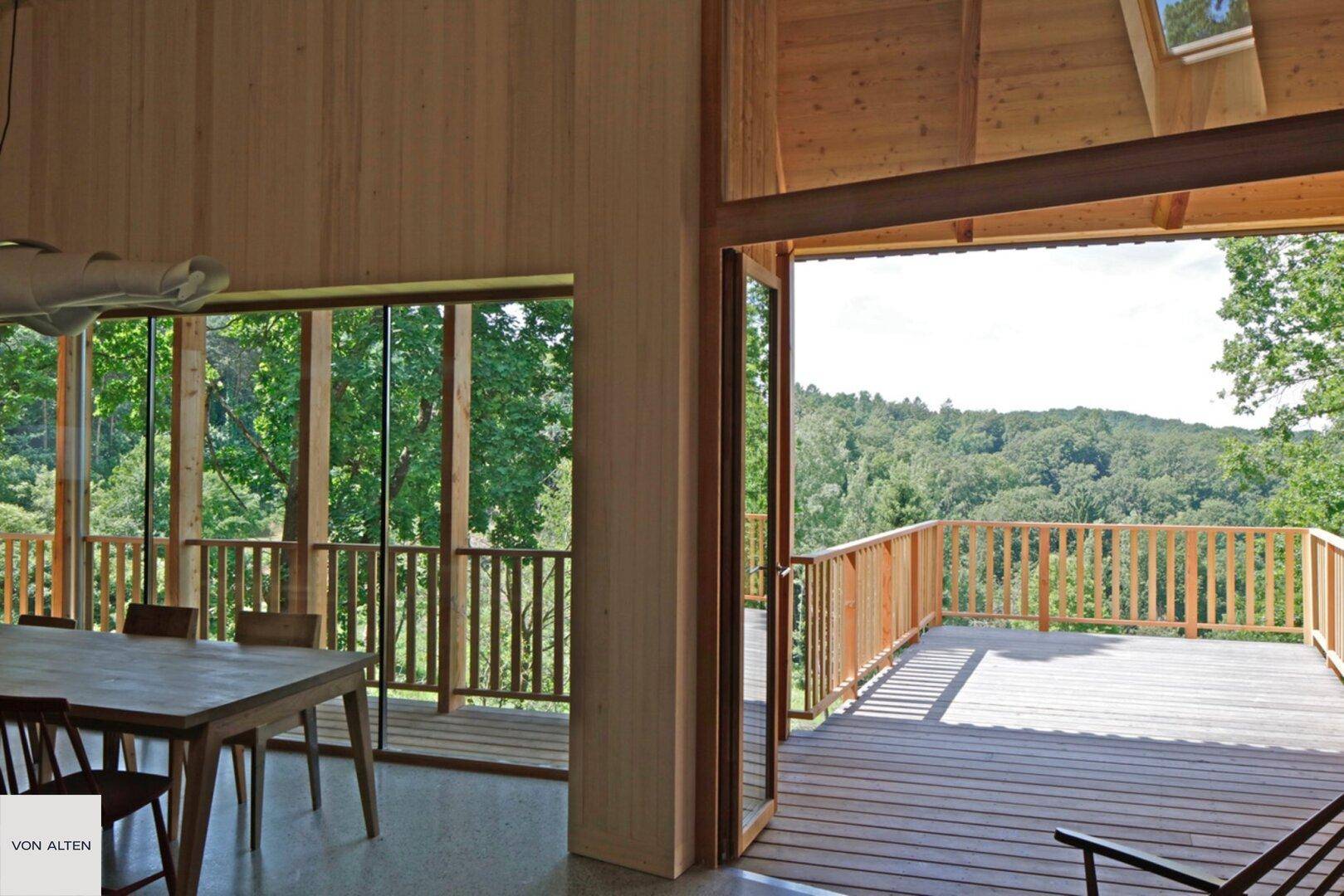 Offener Essbereich mit Zugang zu einer großen Holzterrasse und weitem Waldblick.