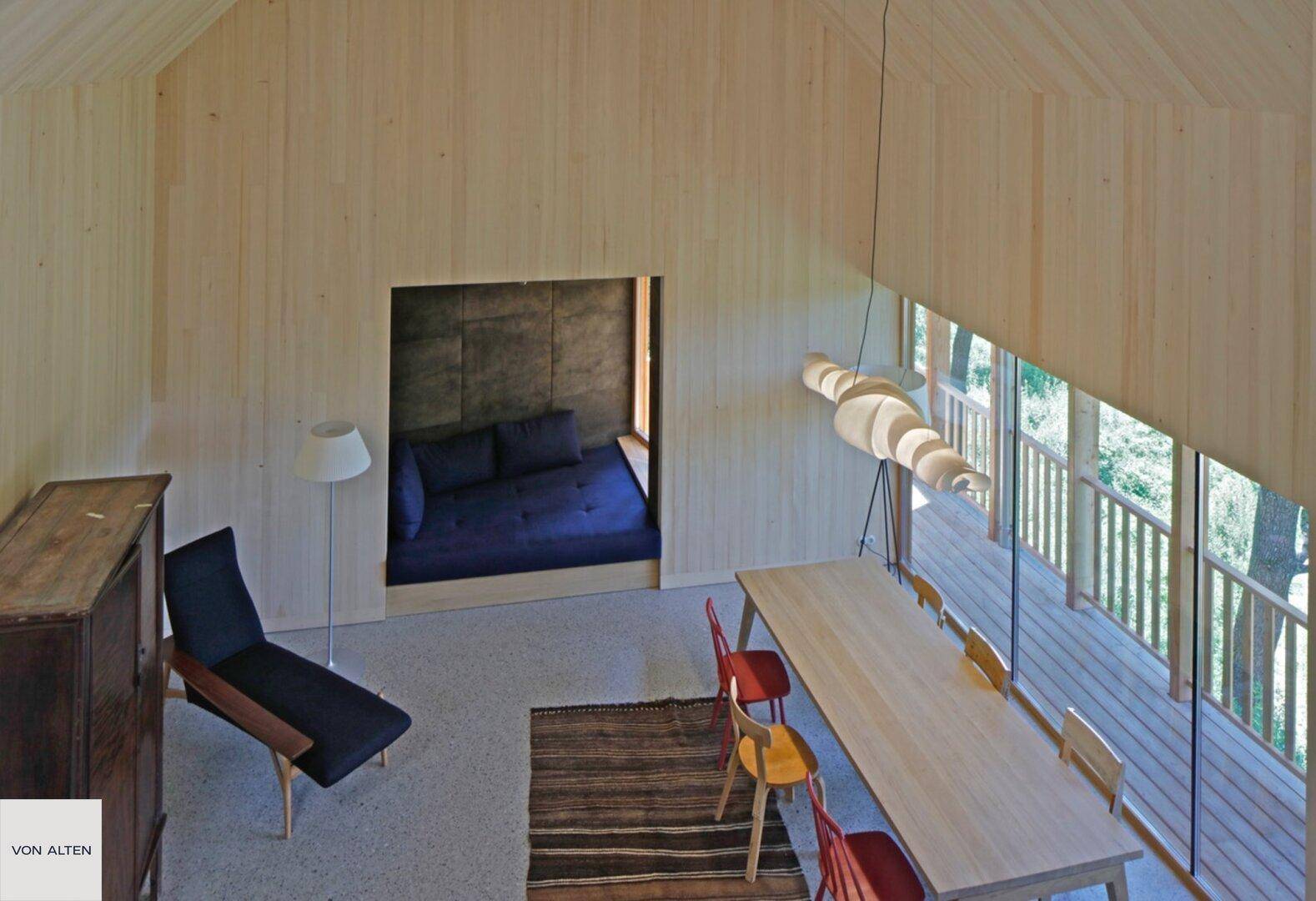Offener Wohn- und Essbereich mit hoher Decke, Holzwänden und gemütlicher Schlafnische.