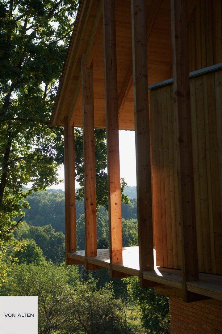 Detailansicht des hölzernen Balkons mit vertikalen Stützen und sonnigem Waldblick.