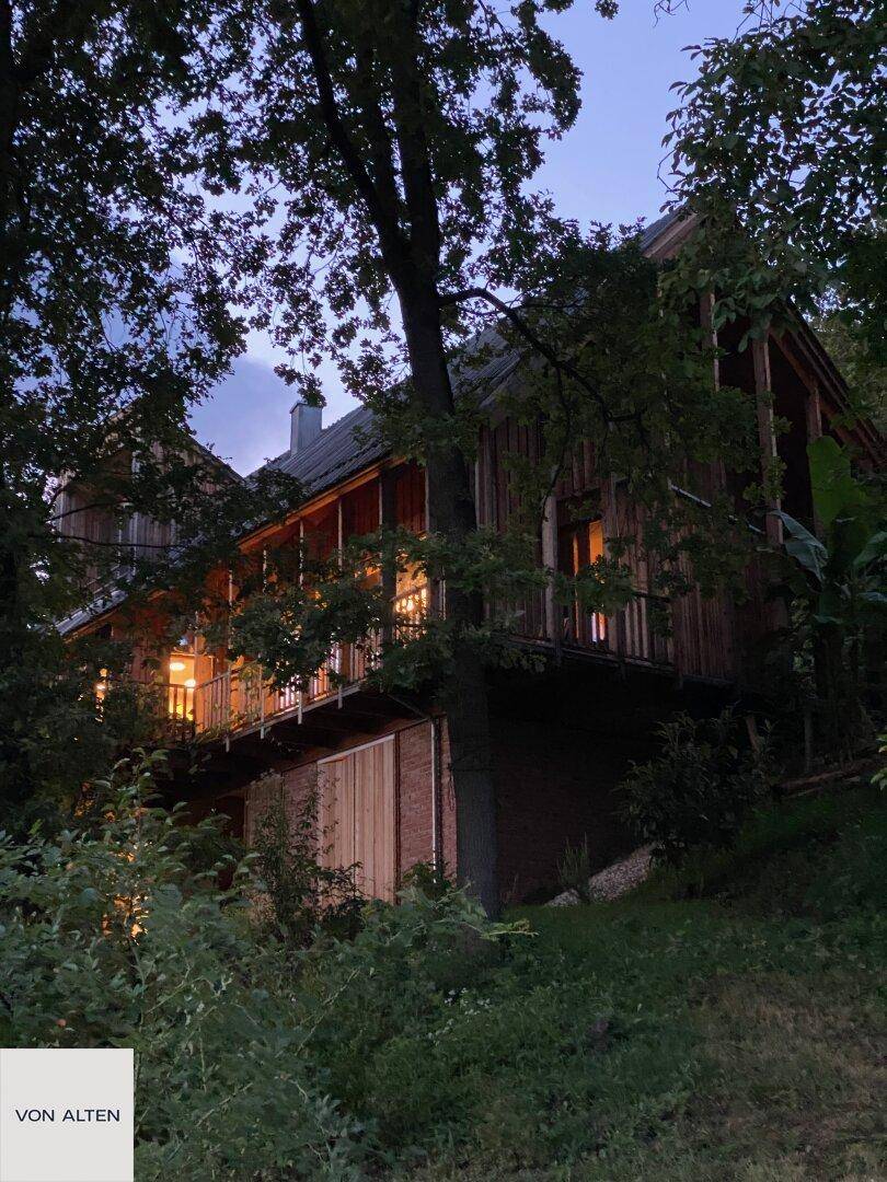Das Holzhaus bei Nacht, warm beleuchtet und eingebettet in die dunkle Waldumgebung.