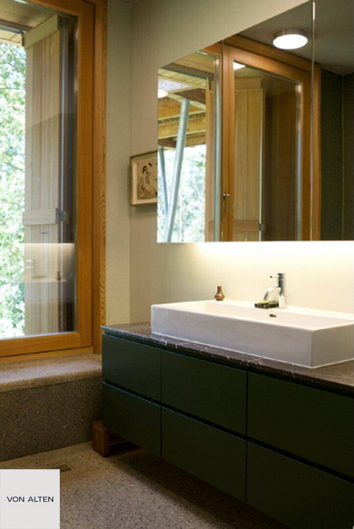 Modernes Badezimmer mit Aufsatzwaschbecken, dunklen Schränken und großem Fenster.