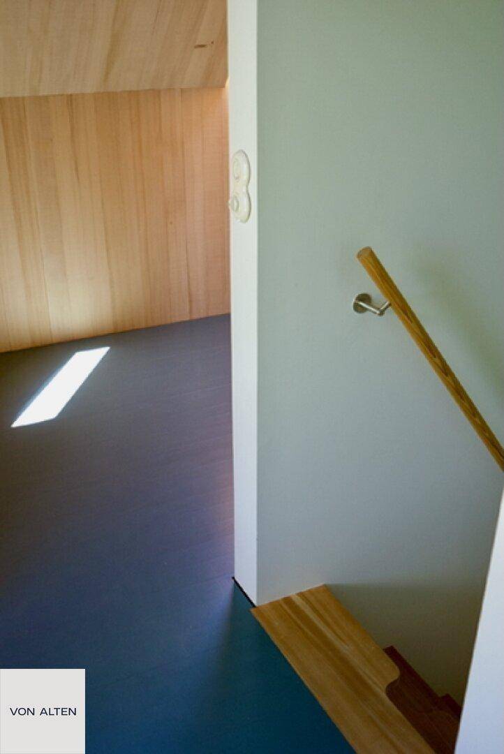 Detailansicht einer Holztreppe und Wand in einem hellen Innenraum.