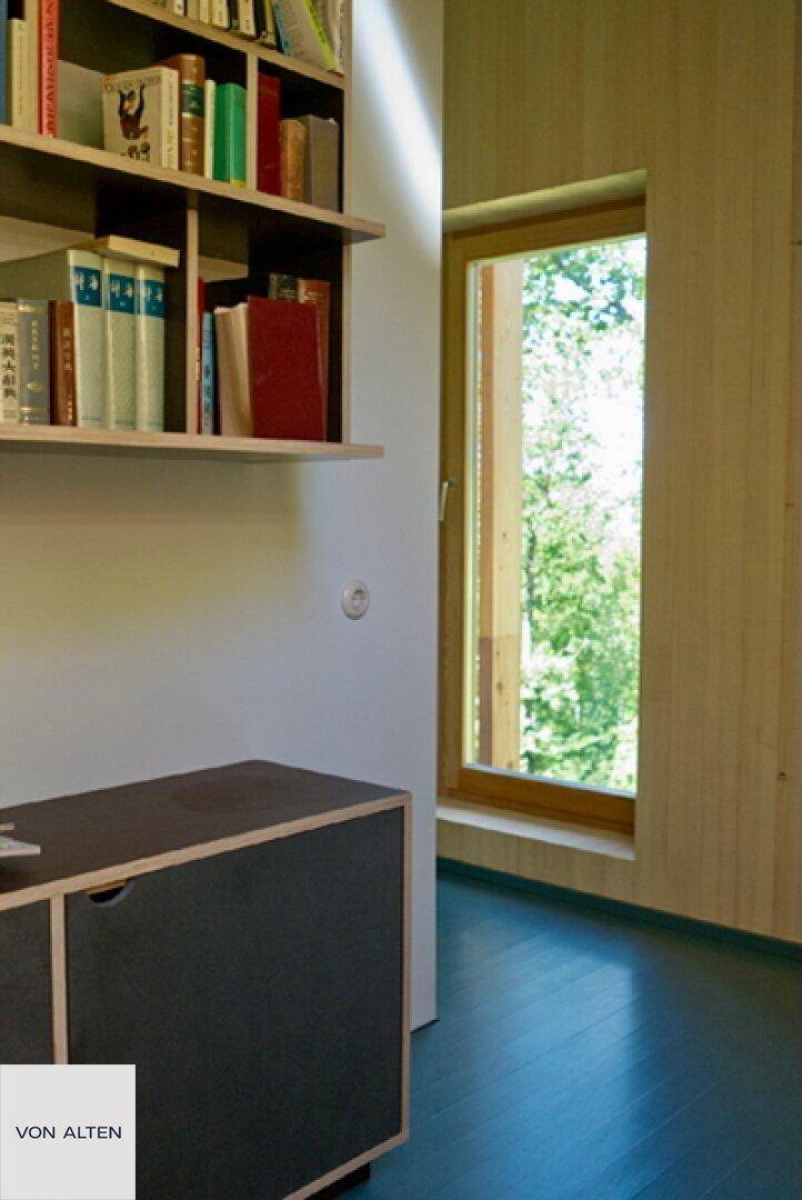 Heller Flurbereich mit Bücherregal, kleinem Schrank und Fenster mit Waldblick.