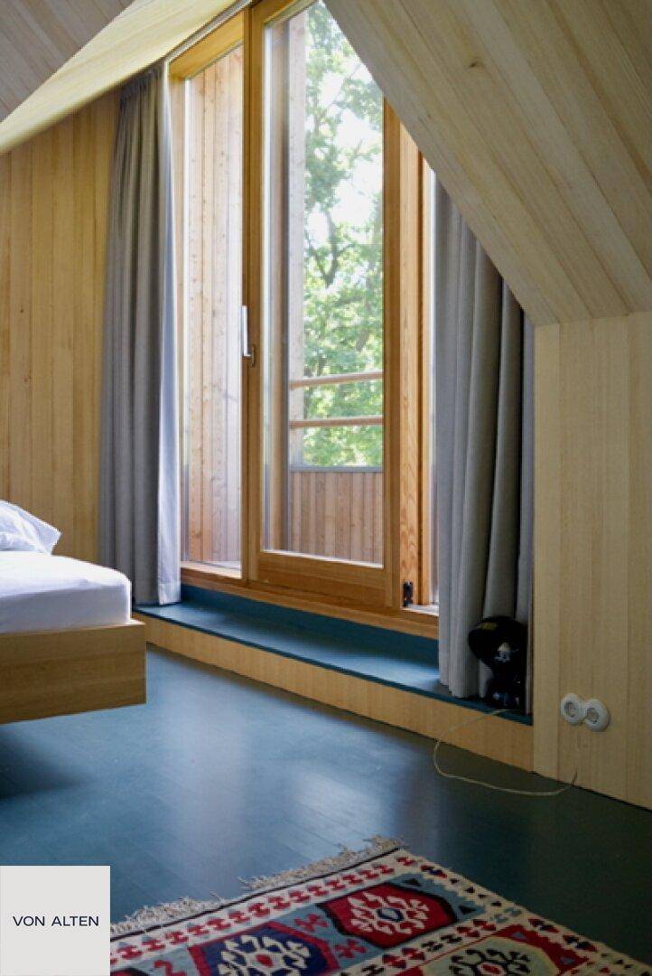 Helles Schlafzimmer mit großem Fenster, schräger Decke und Holzwänden.