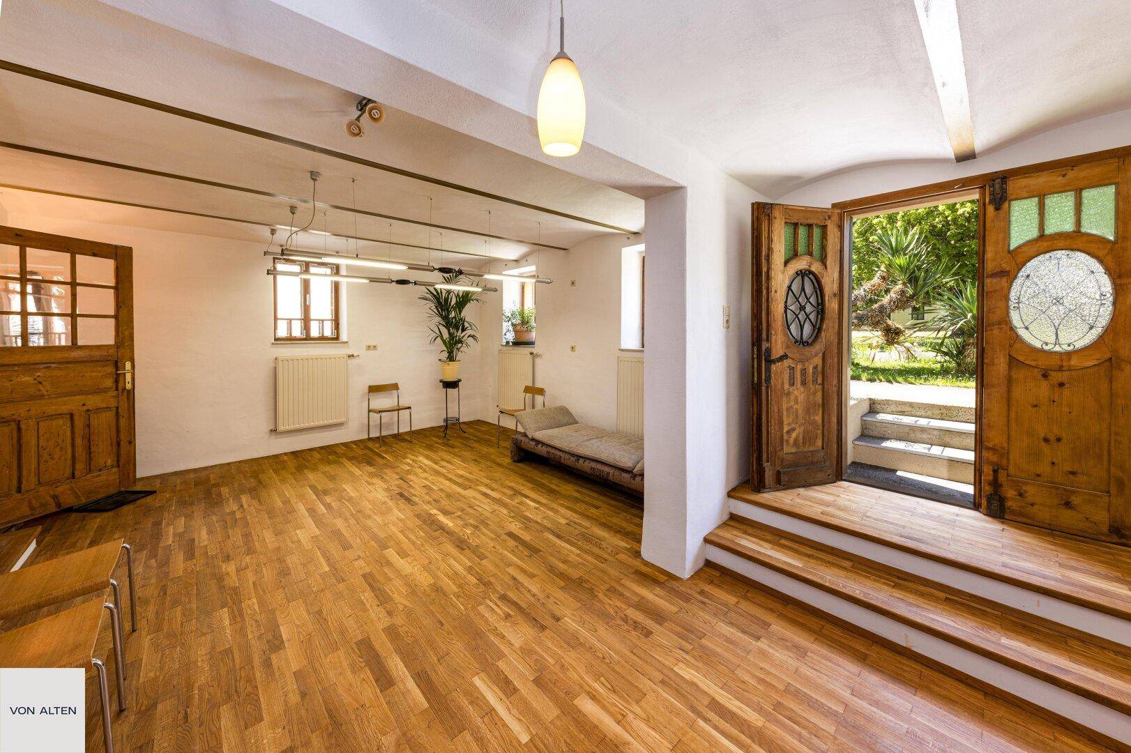Großer Raum mit Holzboden und Zugang zum Garten, ideal für vielfältige Nutzungsmöglichkeiten.