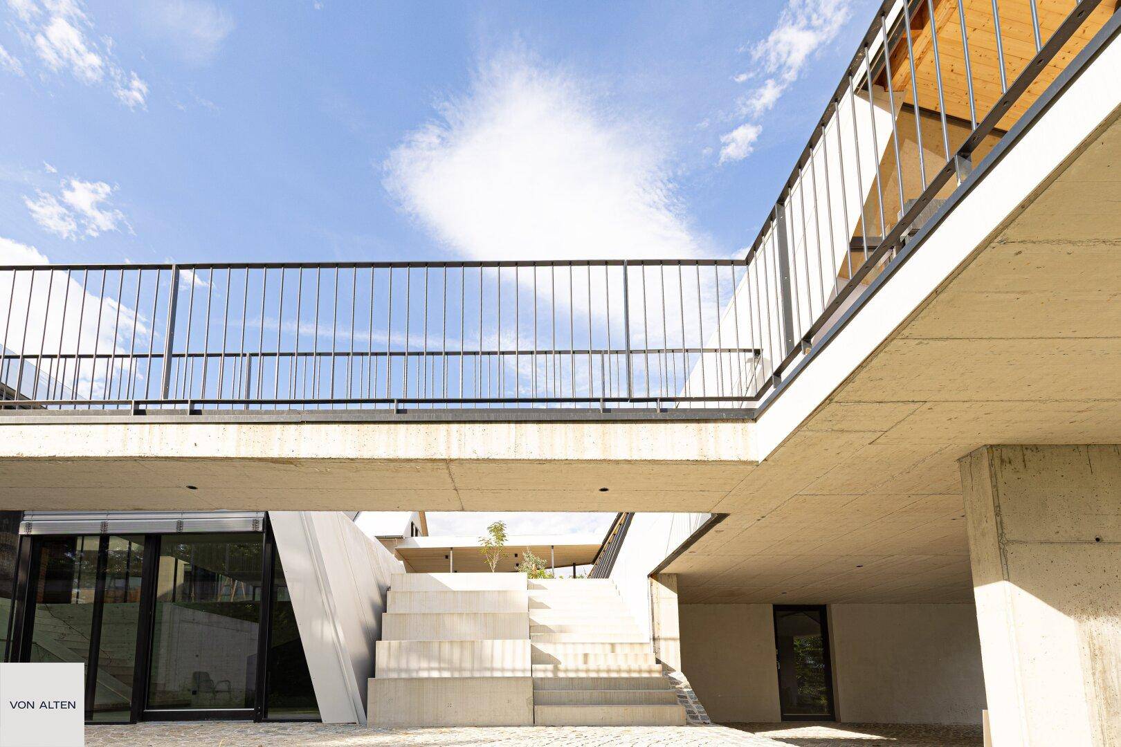 Moderne Architektur mit klaren Linien, Betonstrukturen und einer erhöhten Gehwegbrücke.