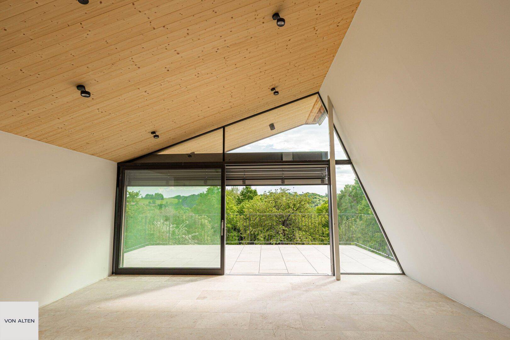 Heller Wohnraum mit schräger Holzdecke und großen Fensterfronten mit Panoramablick.
