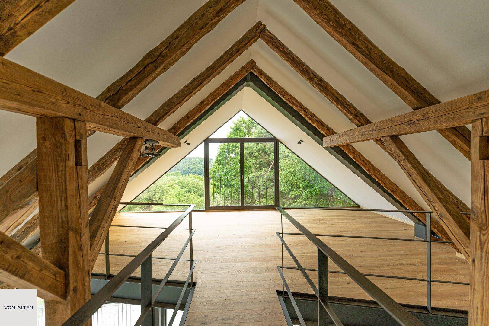 Offene Galerie mit freiliegenden Holzbalken und großem Fenster mit Blick in die Natur.
