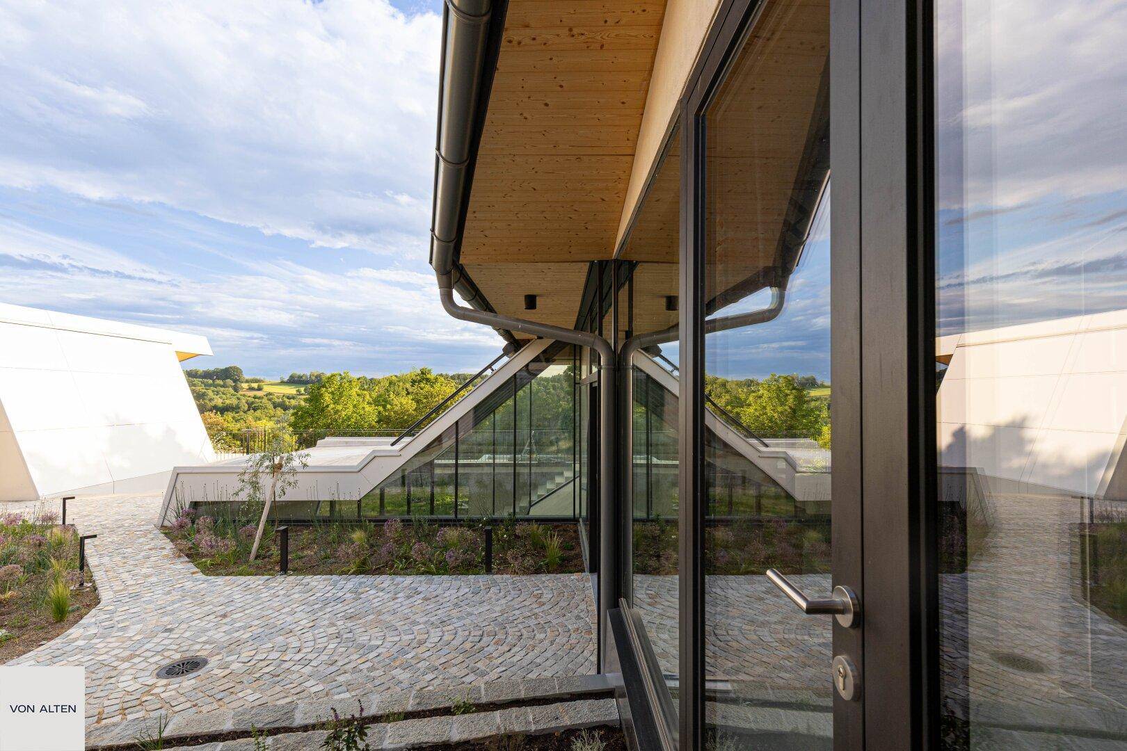 Architektonisch anspruchsvolle Fassade mit großen Glasflächen und Blick auf die grüne Umgebung.