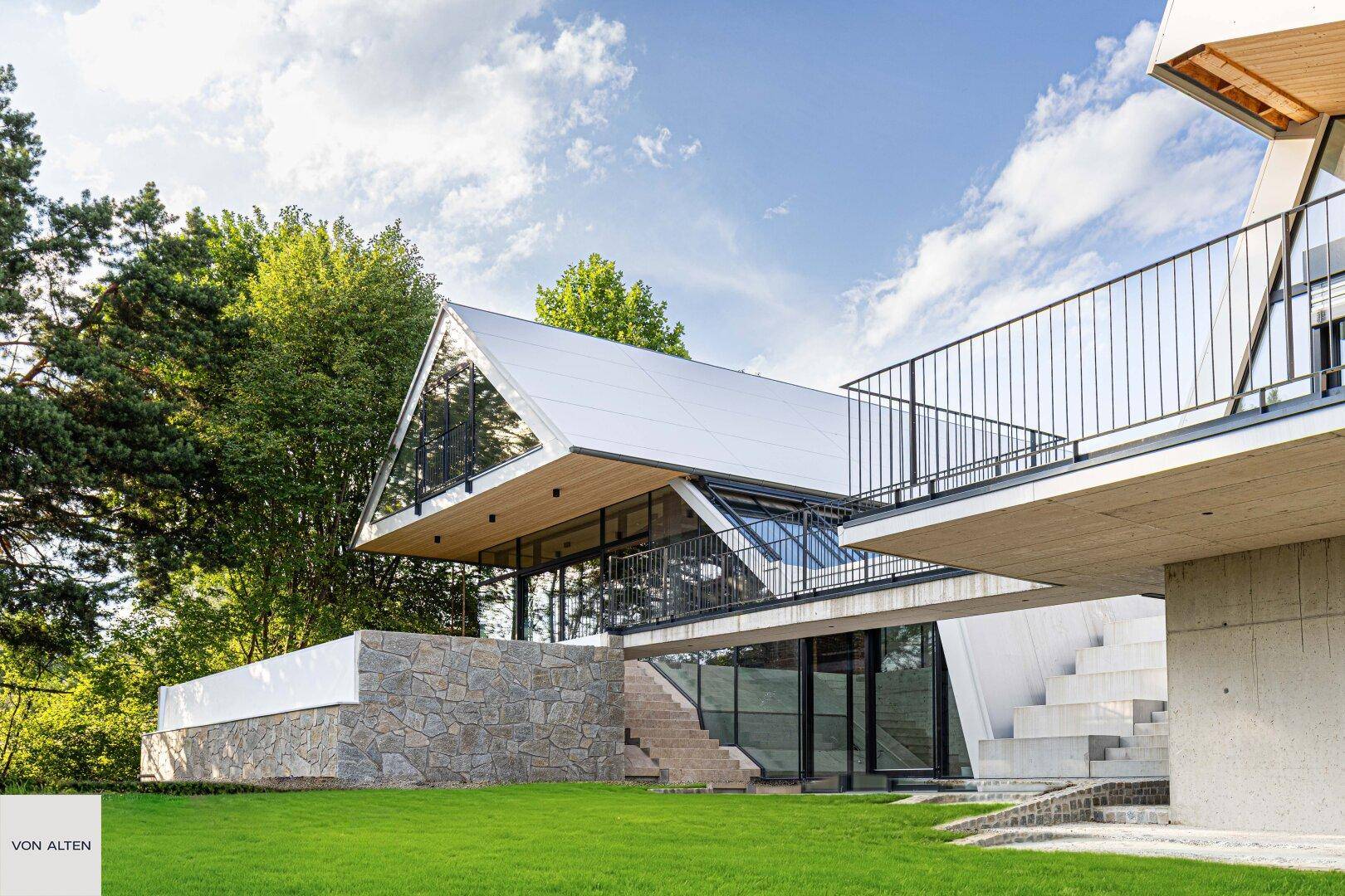 Beeindruckende moderne Architektur mit großen Glasflächen und schwebenden Balkonen inmitten grüner Natur.