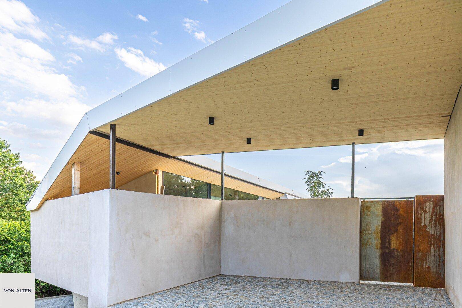 Überdachter Parkbereich mit moderner Holzdecke und einer markanten rostfarbenen Metalltür.