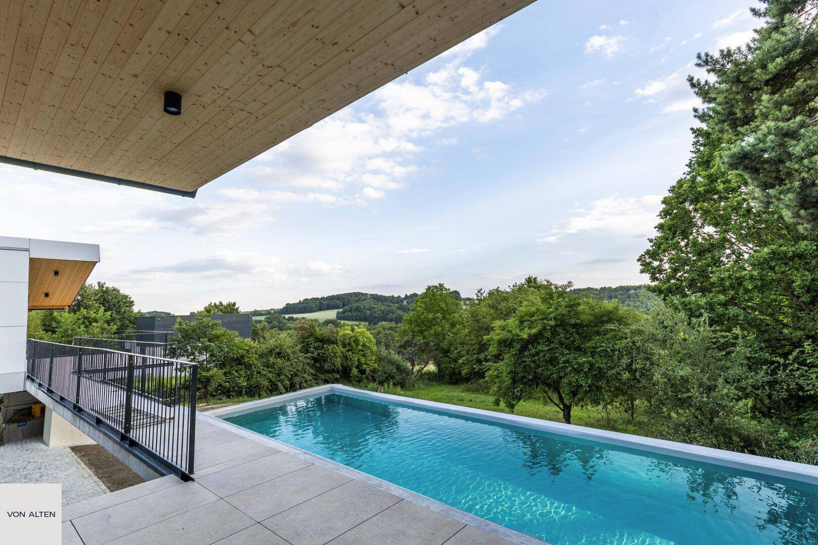 Moderner Infinity-Pool mit weitem Blick über die grüne Landschaft und bewaldete Hügel.