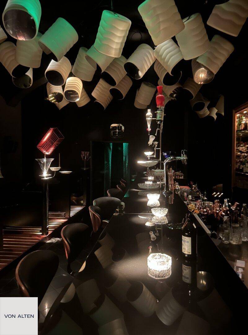 Blick auf die Bar mit dunkler Theke, Barhockern und der charakteristischen Deckenbeleuchtung.
