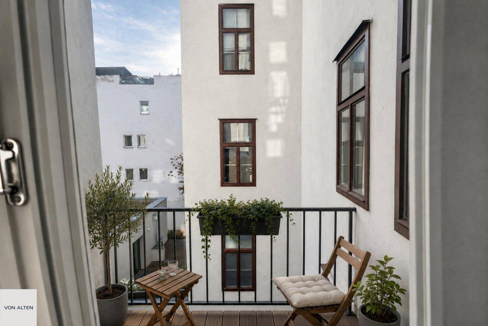 Kleiner Balkon mit Holzboden, Sitzgelegenheiten und Blick auf den ruhigen Innenhof.