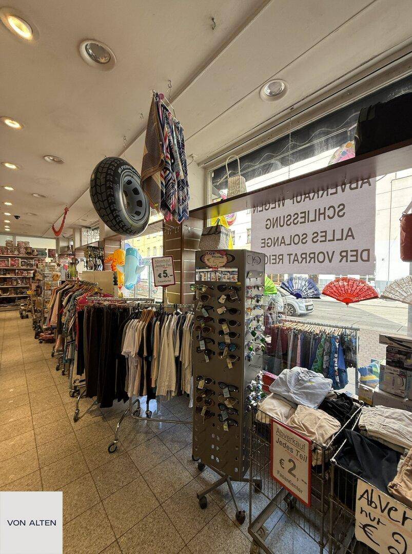 Innenansicht eines Einzelhandelsgeschäfts mit Kleidung, Accessoires und einem Ausverkaufsschild im Schaufensterbereich.