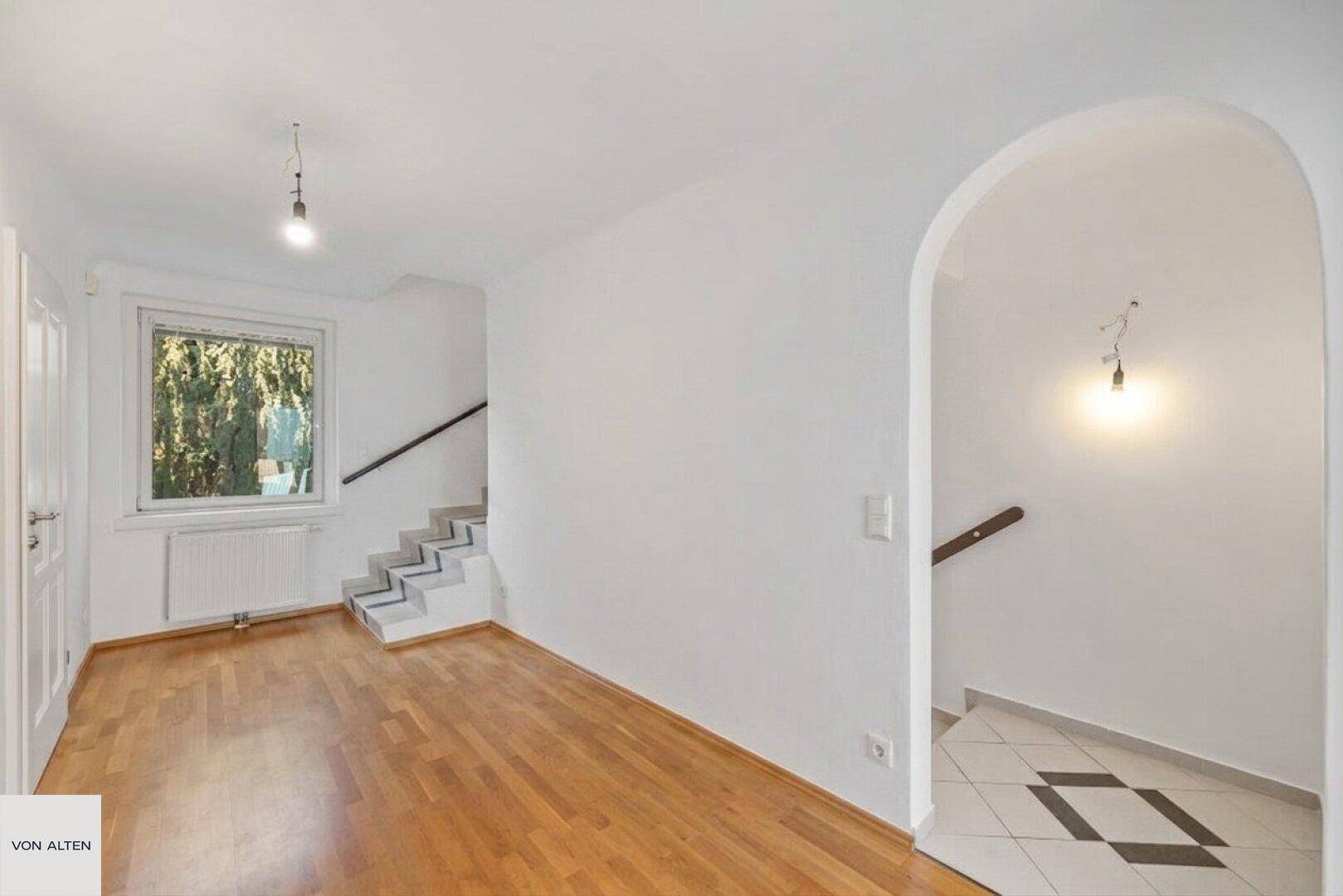 Heller Flur mit Holzfußboden, Treppe und Fenster mit Blick ins Grüne.