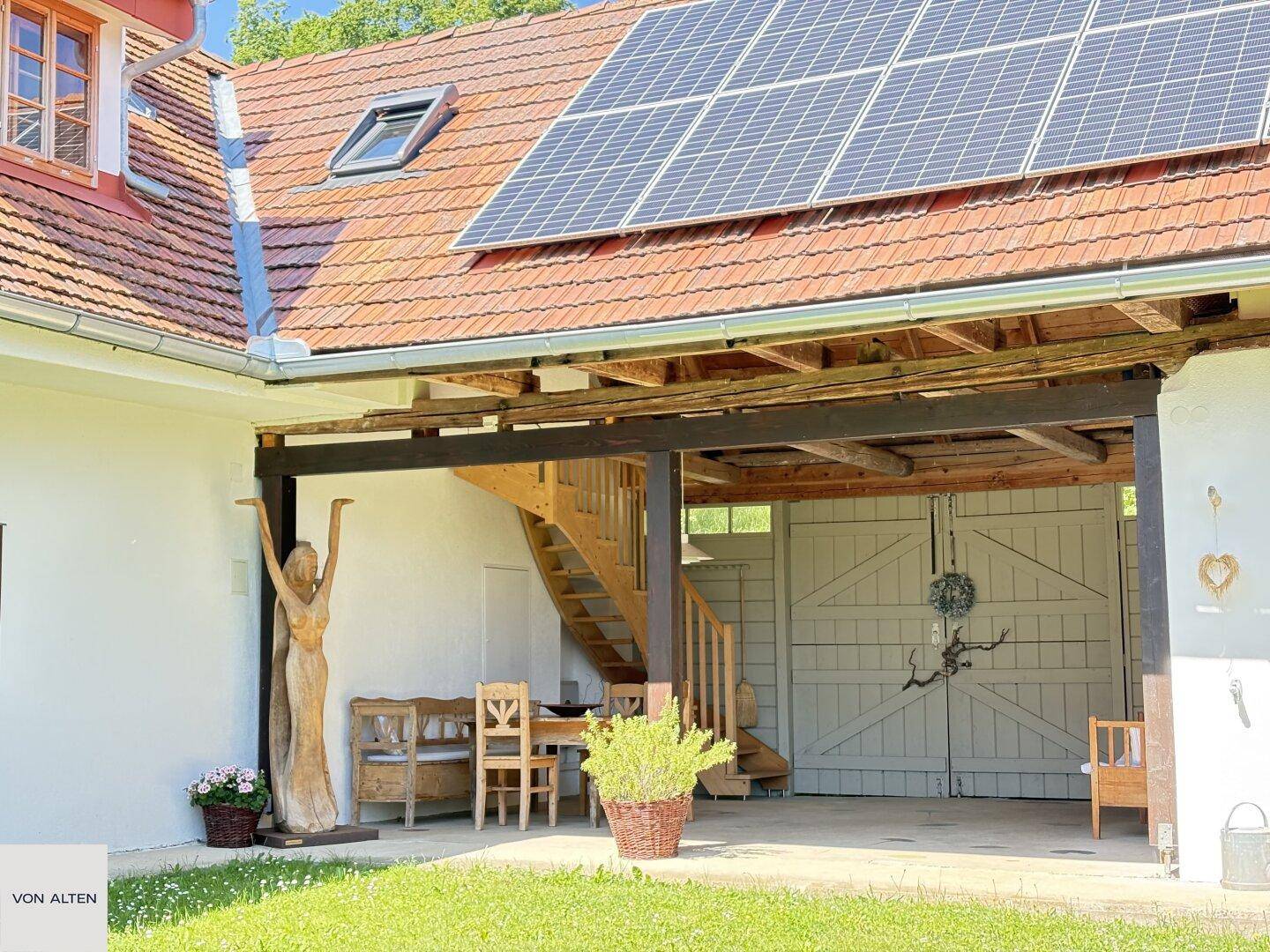 Überdachter Außenbereich mit Holztreppe, Sitzgelegenheiten und Solaranlage auf dem Dach.