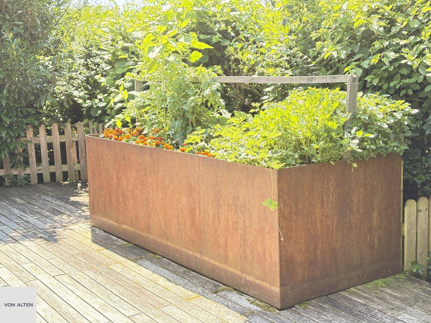 Rustikaler Hochbeet aus Cortenstahl mit verschiedenen Pflanzen auf einer Holzterrasse.