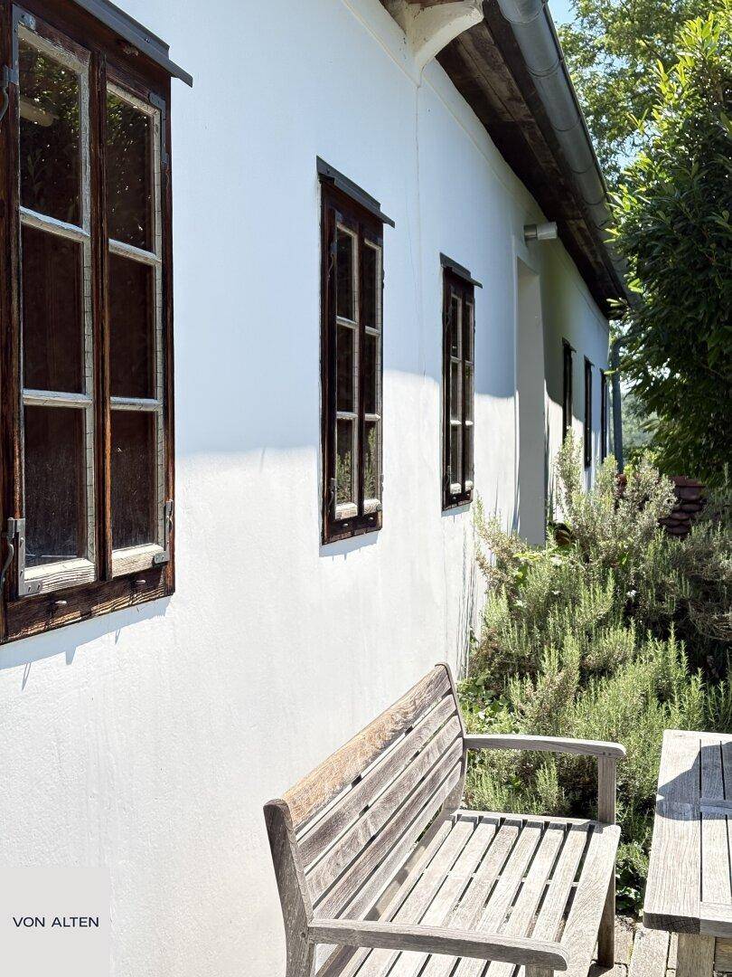 Detailansicht der weißen Fassade eines alten Bauernhauses mit rustikalen Holzfenstern und Sitzbank.