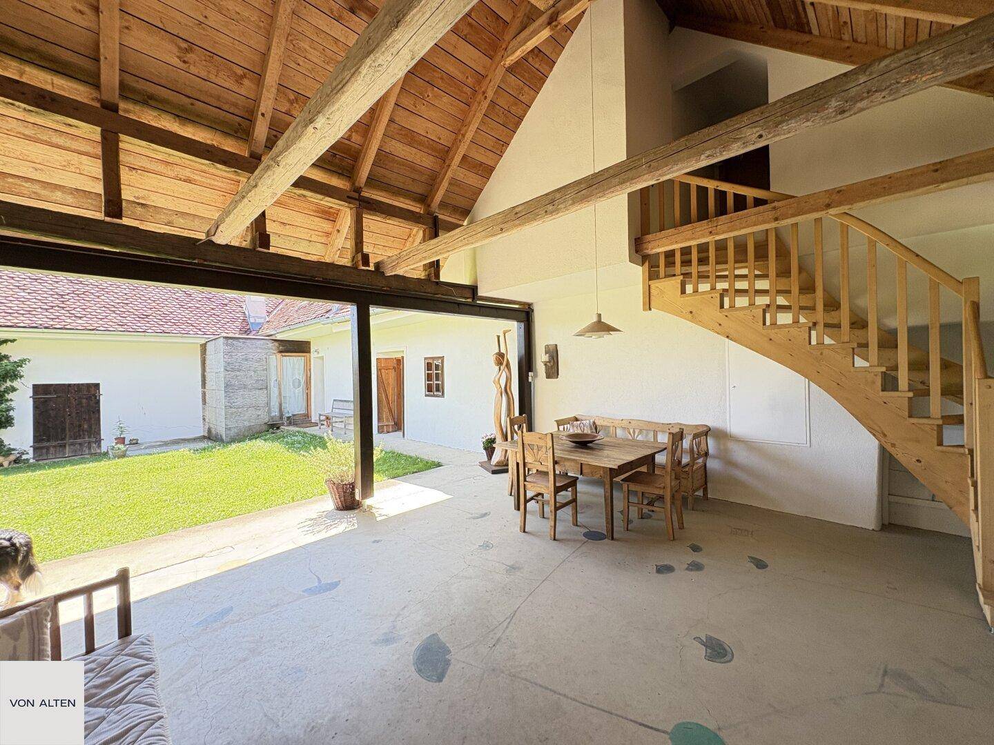Offener Wohn- und Essbereich mit Holzbalken, rustikalen Möbeln und Blick in den Garten.