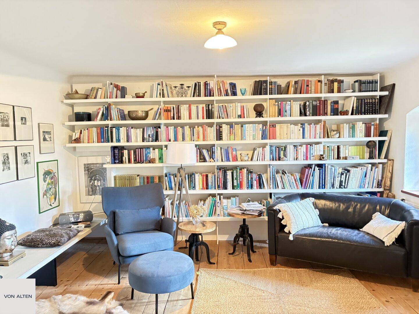 Helles Wohnzimmer mit großer Bücherwand, Ledersofa und bequemen Sitzgelegenheiten.