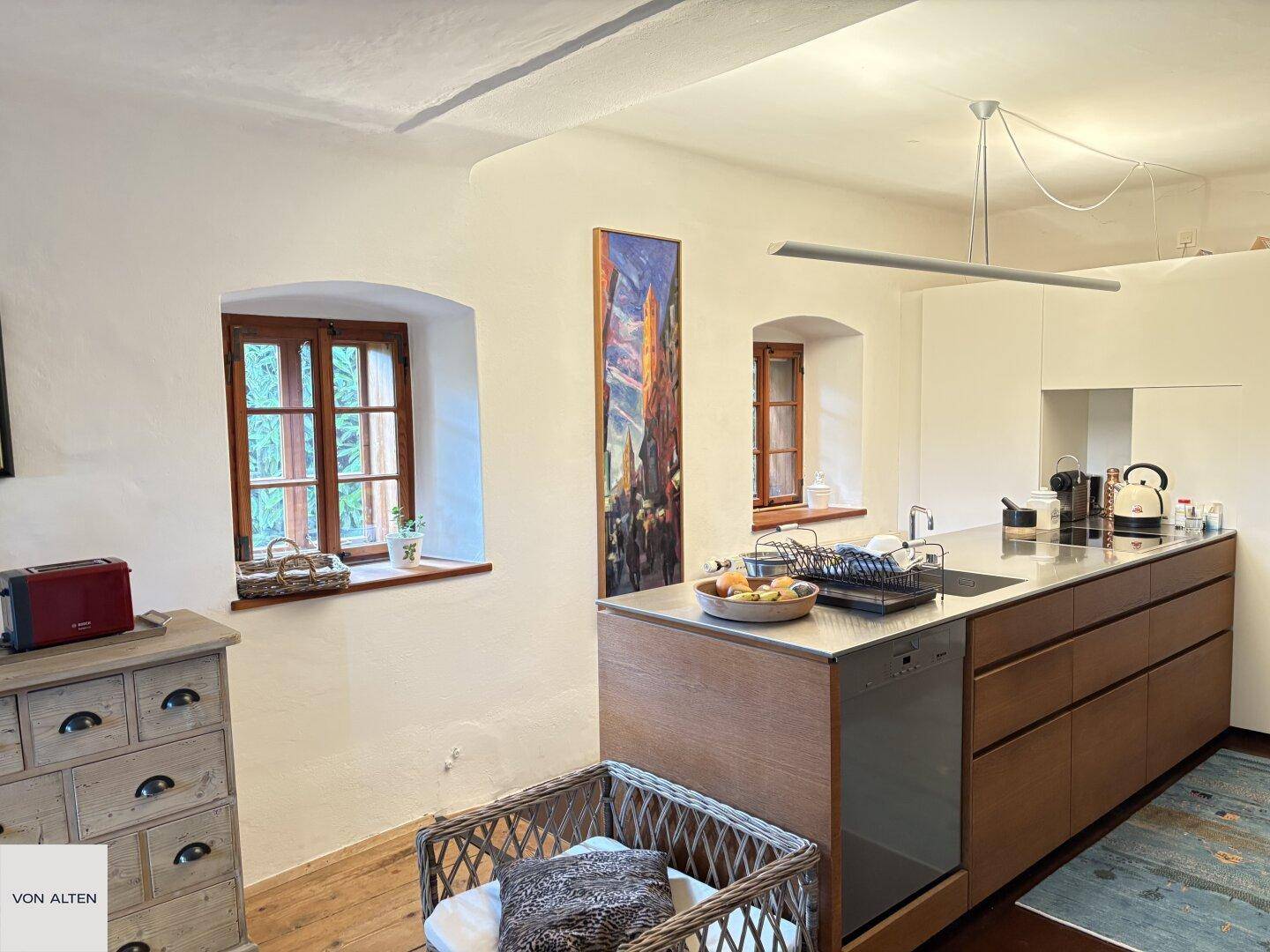 Moderne Küche mit Holzfronten, Edelstahl-Arbeitsplatte und rustikalen Fenstern.
