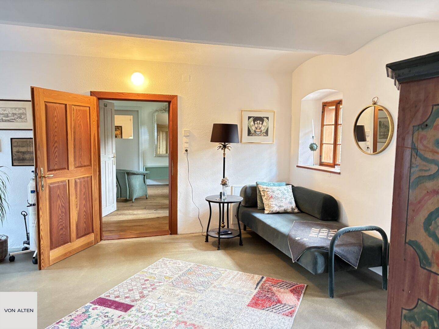 Helles Zimmer mit Tagesbett, farbenfrohem Teppich und Holztüren.
