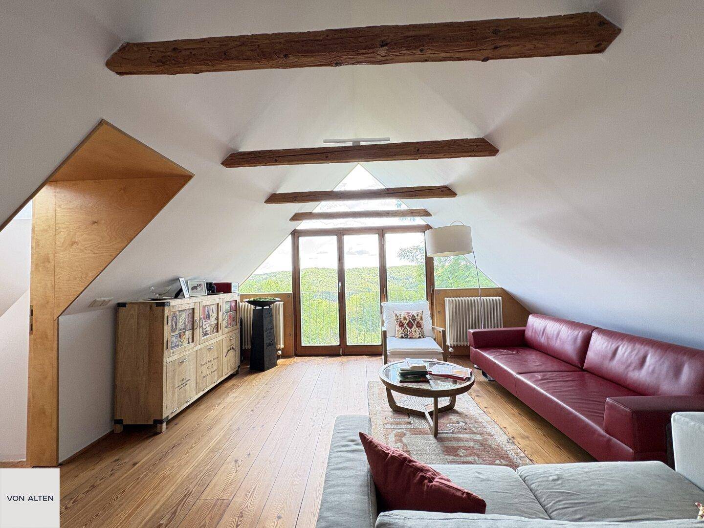 Helles Dachgeschoss-Wohnzimmer mit rotem Sofa, Holzboden und großen Fenstern mit Panoramablick.