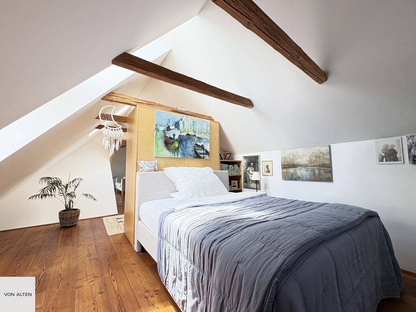 Gemütliches Schlafzimmer im Dachgeschoss mit Holzboden, sichtbaren Balken und schrägen Wänden.
