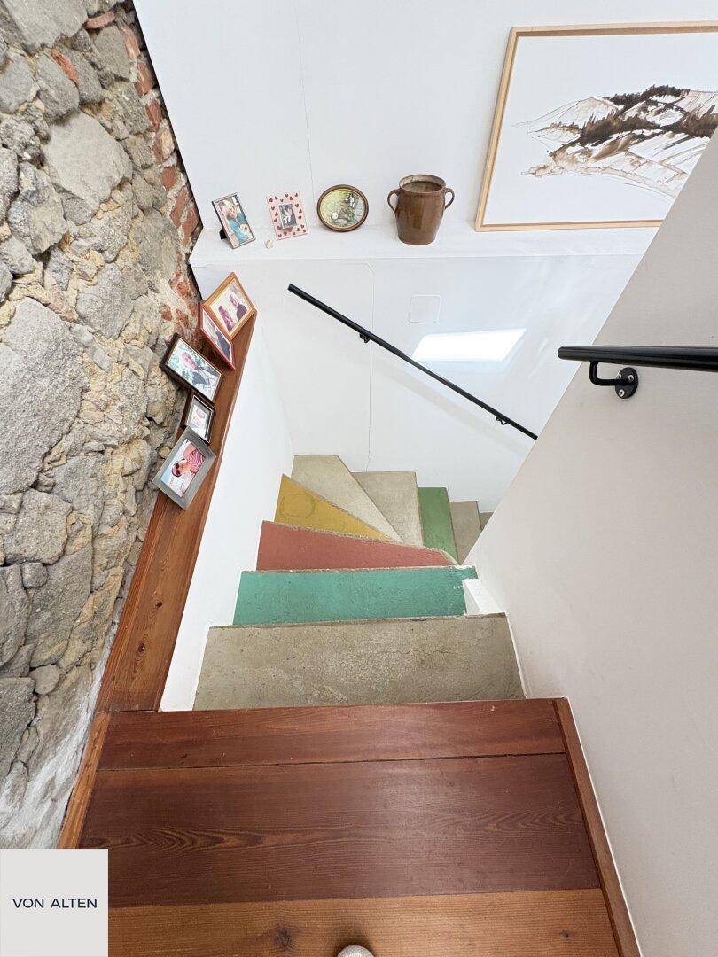 Bunte Treppe mit Holzstufen und einer rustikalen Steinwand, die zu den oberen Etagen führt.
